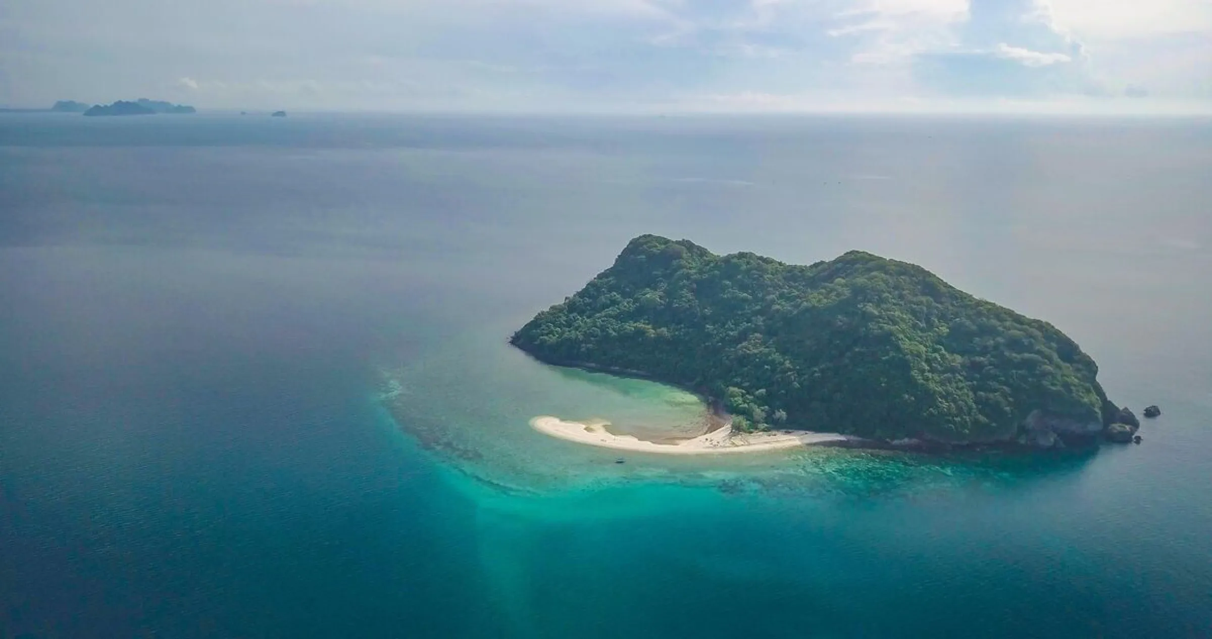 Aerial view of Koh Kye, a jungle covered island ringed by a white coral sand beach and turquoise sea.