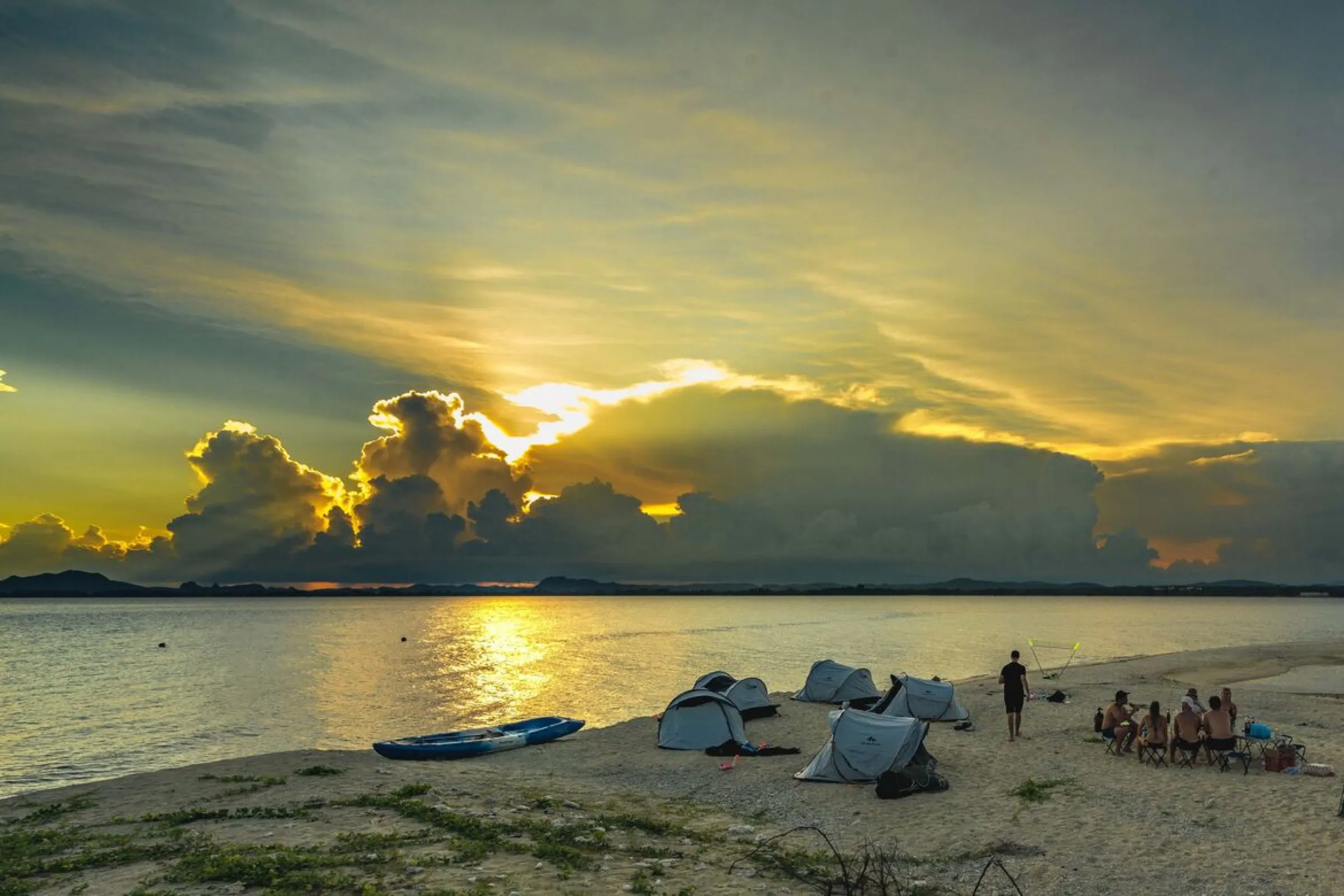 Golden sunset over the camp on Koh Kye, with tents, a kayak and the group on the shore.