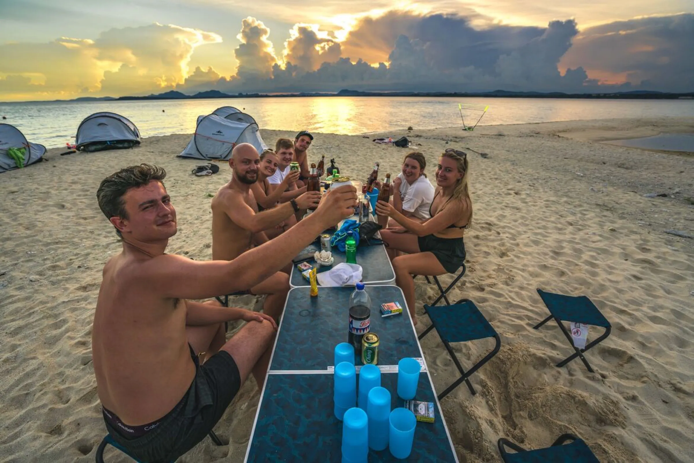 The group raising a toast around the table on the beach at sunset.