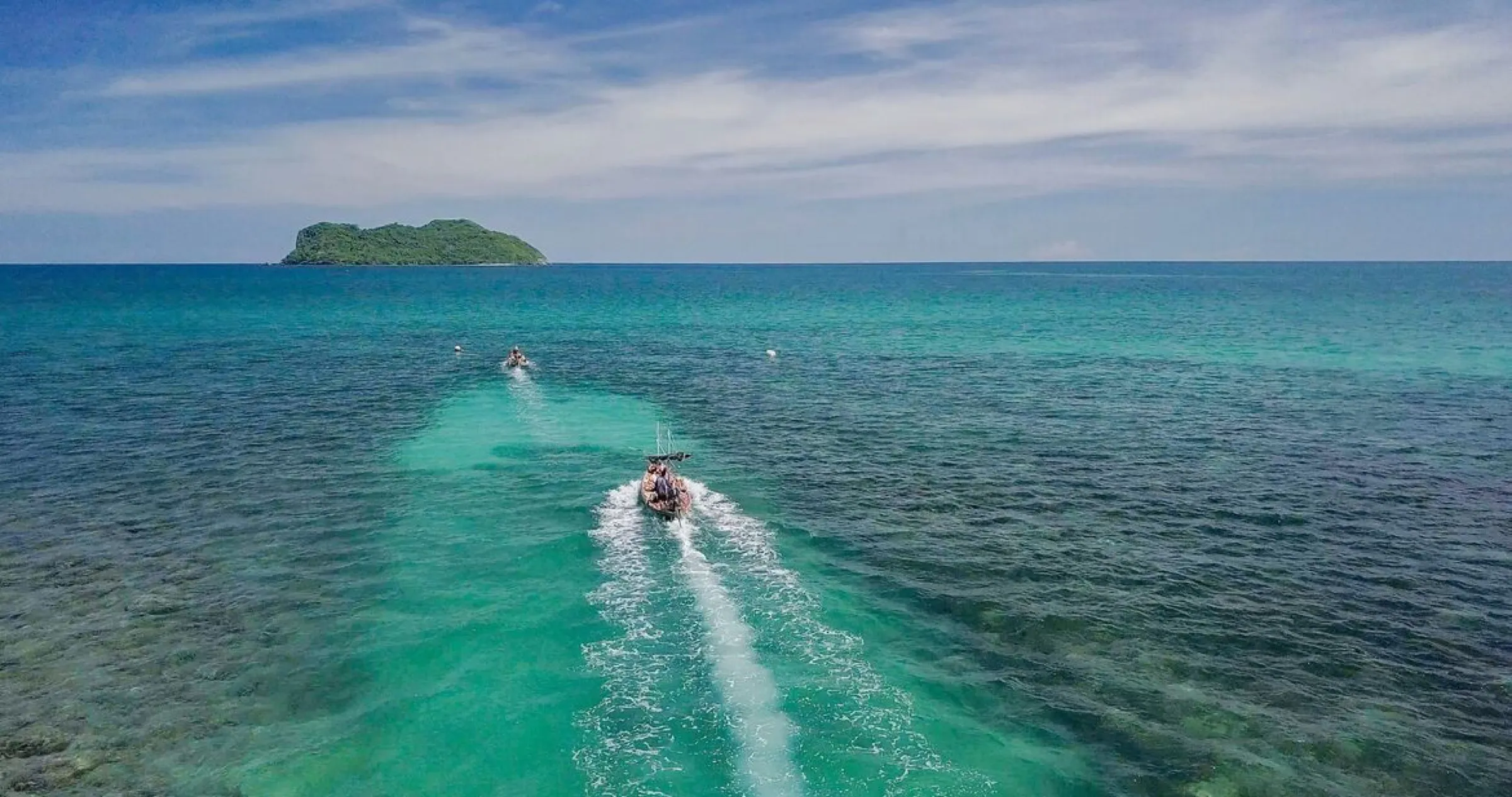Longtail boats speeding across turquoise water toward the island.
