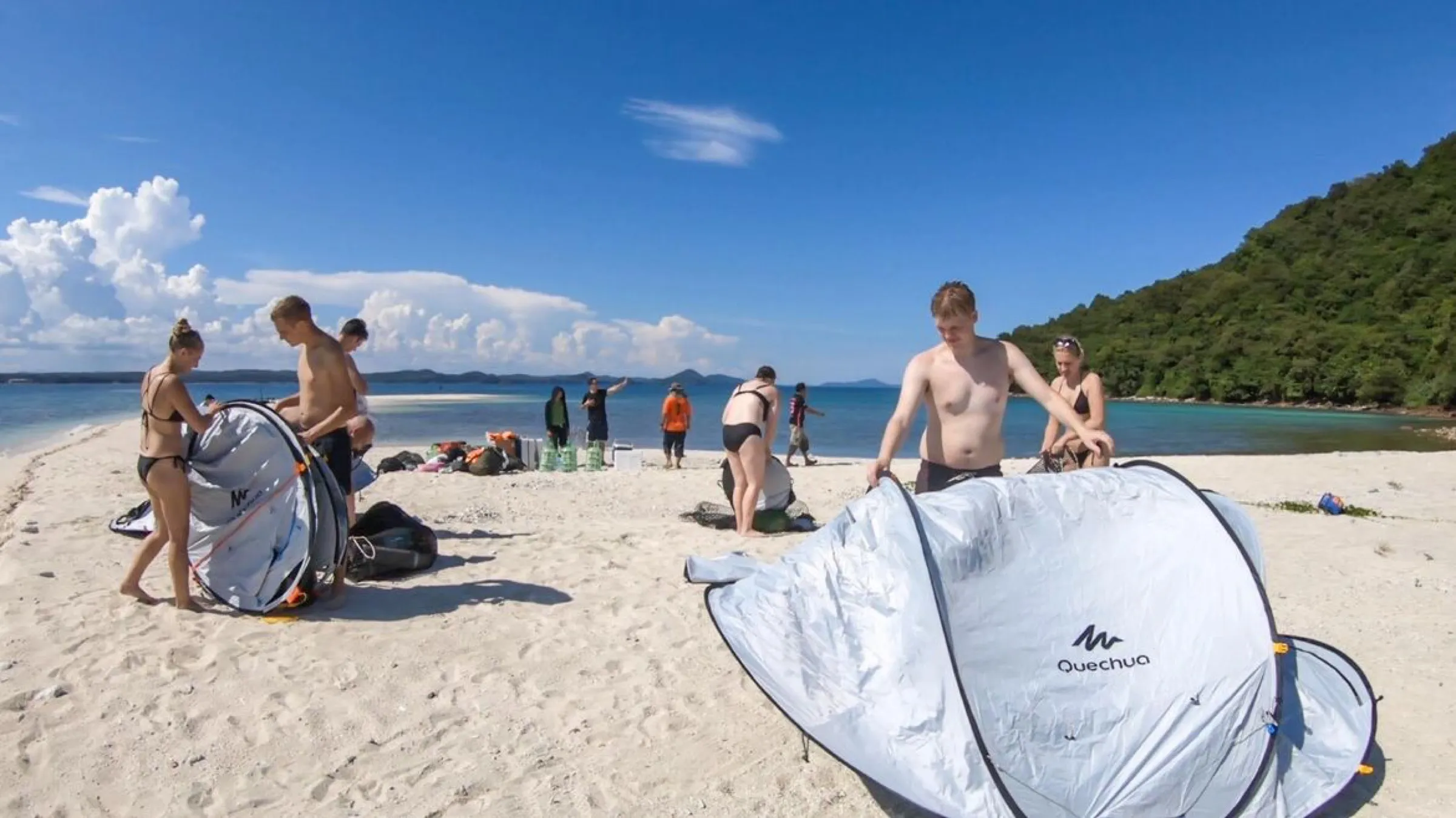 The group pitching pop up tents on the bright white beach under a blue sky.