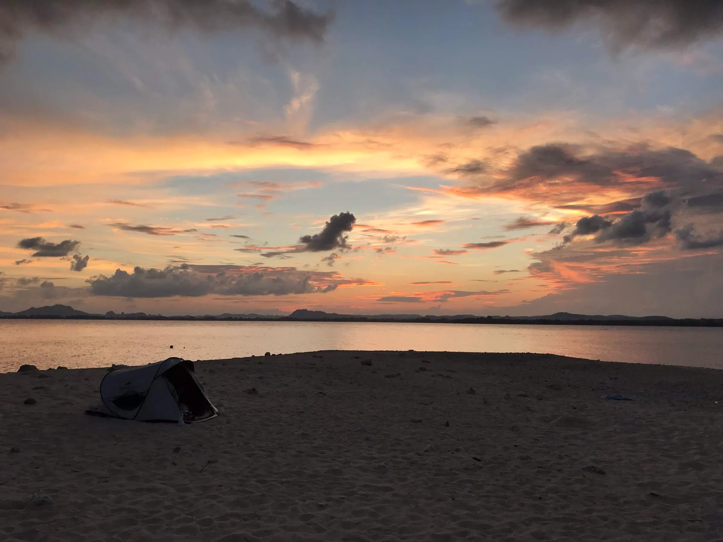 A single tent on the white sand spit of Koh Kye beneath a dramatic painted sunset sky.